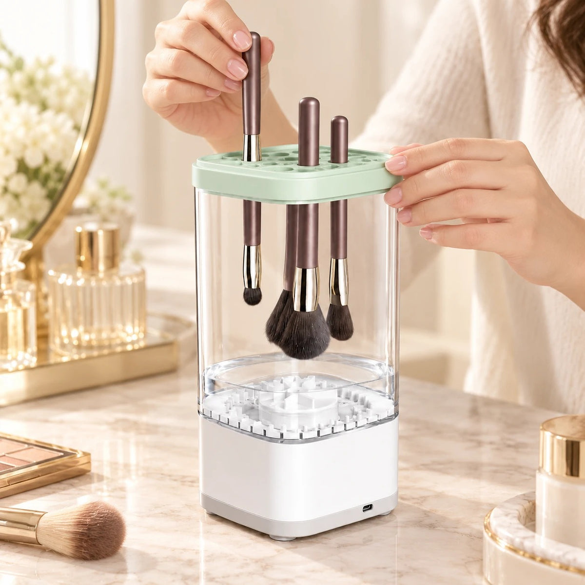 Manos colocando brochas de maquillaje en la tapa del limpiador eléctrico
